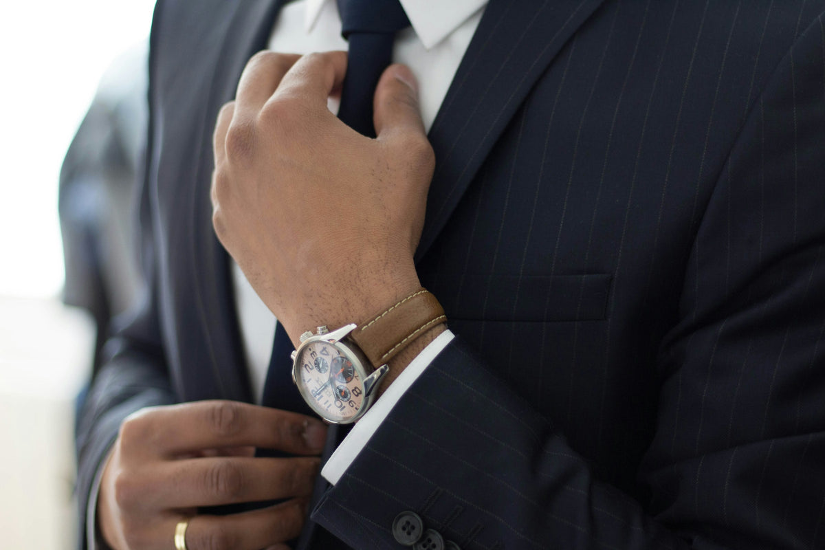 Man in a navy suit adjusting his tie, an automatic watch on his wrist
